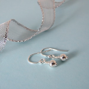 May include: A pair of silver dangle earrings with small round balls at the end. The earrings are on a light blue background.