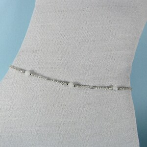 Op de afbeelding: Een zilveren body chain met witte kralen. De ketting is delicaat en heeft een eenvoudig ontwerp.