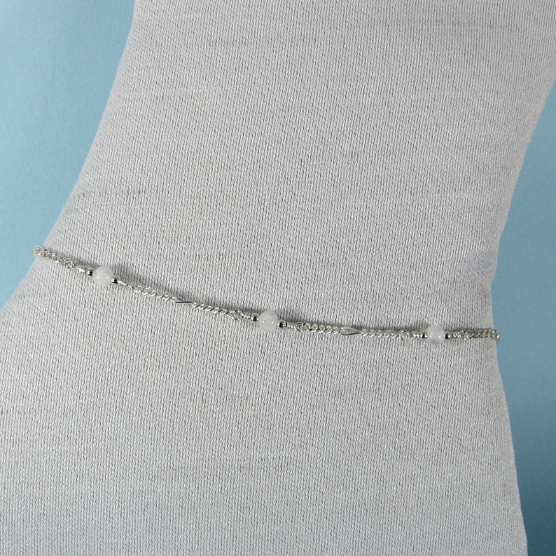 Op de afbeelding: Een zilveren body chain met witte kralen. De ketting is delicaat en heeft een eenvoudig ontwerp.
