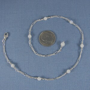 Op de afbeelding: Een zilveren enkelketting met witte maansteen kralen. De enkelketting is ongeveer zo groot als een dubbeltje.
