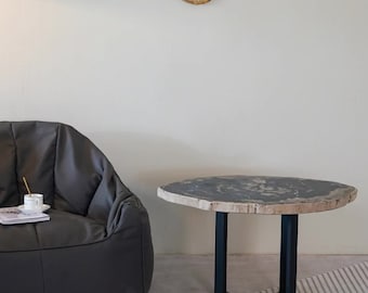 May include: A round, black and white petrified wood coffee table with a black metal base. The table is sitting on a gray and white patterned rug in front of a gray couch.