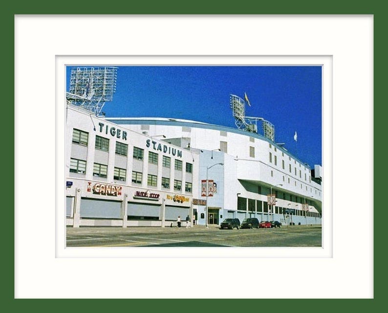 May include: A vintage photograph of Tiger Stadium in Detroit, Michigan. The stadium is white with a blue sky in the background. The words "Tiger Stadium" are visible on the side of the building.