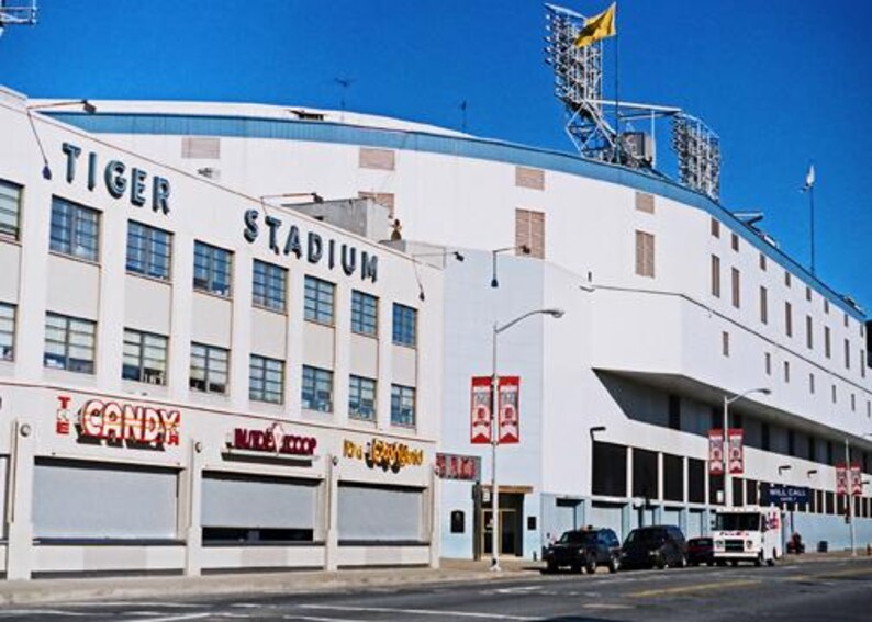 May include: An exterior view of Tiger Stadium, a large white building with blue trim and the words "Tiger Stadium" in blue lettering. The stadium has many windows and a large sign that says "Candy" in red and white lettering.