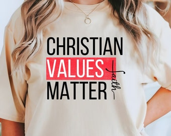 May include: A beige t-shirt with the text "Christian Values Matter" in black lettering. The word "Values" is in red and the text "with Faith" is written vertically on the right side of the shirt.