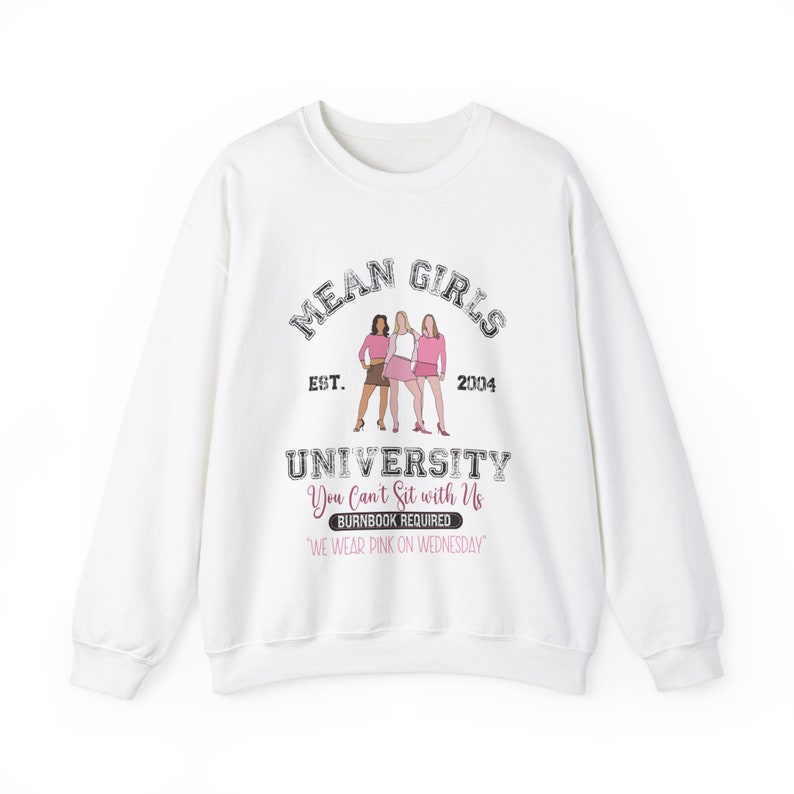 Pu&ograve; includere: Felpa bianca con una stampa grafica di tre ragazze in abiti rosa. Il testo recita "Mean Girls University Est. 2004 You Can't Sit with Us Burnbook Required 'We Wear Pink on Wednesday'"