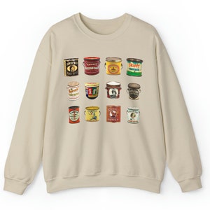 May include: A beige sweatshirt with a vintage design featuring a grid of 15 different peanut butter jar labels. The labels are in various colors and feature different brand names and illustrations.