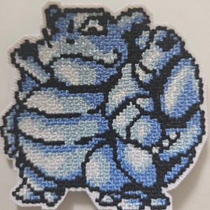 Könnte beinhalten: Blau-weißer gestickter Aufnäher mit einer Comicfigur. Die Figur ist eine blaue und weiße Kreatur mit einem runden Körper und einem kleinen Kopf. Die Figur steht auf ihren Hinterbeinen und hat ihre Arme in die Luft erhoben.