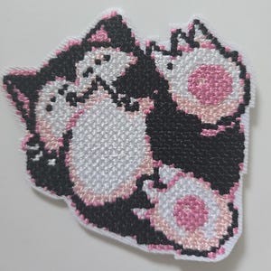 May include: Embroidered patch featuring three black and white cats with pink accents. The cats are in a playful pose, with one cat on top of the other two. The patch is ideal for adding a touch of whimsy to any project.