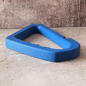 Könnte beinhalten: Ein leuchtend blaues, rechteckiges Objekt mit strukturierter Oberfläche. Das Objekt hat eine dreieckige Öffnung in der Mitte und scheint aus einem festen Material zu bestehen. Der Artikel ist vor einem neutralen Hintergrund platziert.