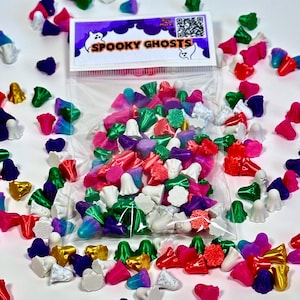 Può includere: Un sacchetto trasparente pieno di caramelle colorate a forma di fantasma. Le caramelle sono in vari colori, tra cui bianco, rosa, verde e viola. Un'etichetta sulla borsa recita "Spooky Ghosts".