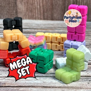 Op de afbeelding: Een verzameling kleurrijke fidget cubes in verschillende kleuren, waaronder roze, groen, geel en zwart. De kubussen zijn in verschillende vormen gerangschikt. De tekst "MEGA SET" staat in een rode explosie.