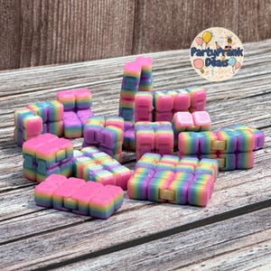 K&ouml;nnte beinhalten: Eine Sammlung farbenfroher, regenbogenfarbener Zappelspielzeuge in verschiedenen Formen. Die Spielzeuge sind haupts&auml;chlich rosa, lila, gelb und blau, angeordnet auf einer Holzoberfl&auml;che. Die Spielzeuge sind zum Manipulieren und Spielen konzipiert.