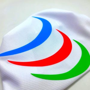 Op de afbeelding: Witte sportstof met een ontwerp van blauwe, rode en groene curven. Het ontwerp bestaat uit drie gebogen vormen in heldere kleuren, die over elkaar zijn geplaatst. De stof heeft een getextureerde, ademende weefsel.