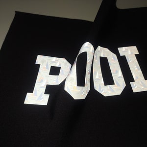 May include: Black fabric with the word "POOL" printed in white reflective letters. The letters are covered in a pattern of small sailboats.
