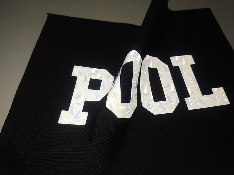 May include: Black fabric with the word "POOL" printed in white reflective letters. The letters are covered in a pattern of small sailboats.