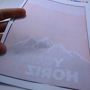 May include: A white print on a pink background with a mountain range and the text "HORIZ YOUR" in white.