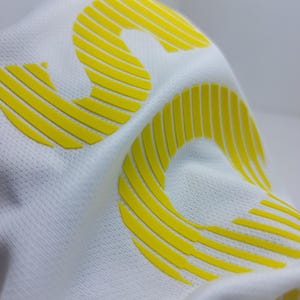 May include: White fabric with a yellow, raised, stylized number "3" printed on it.