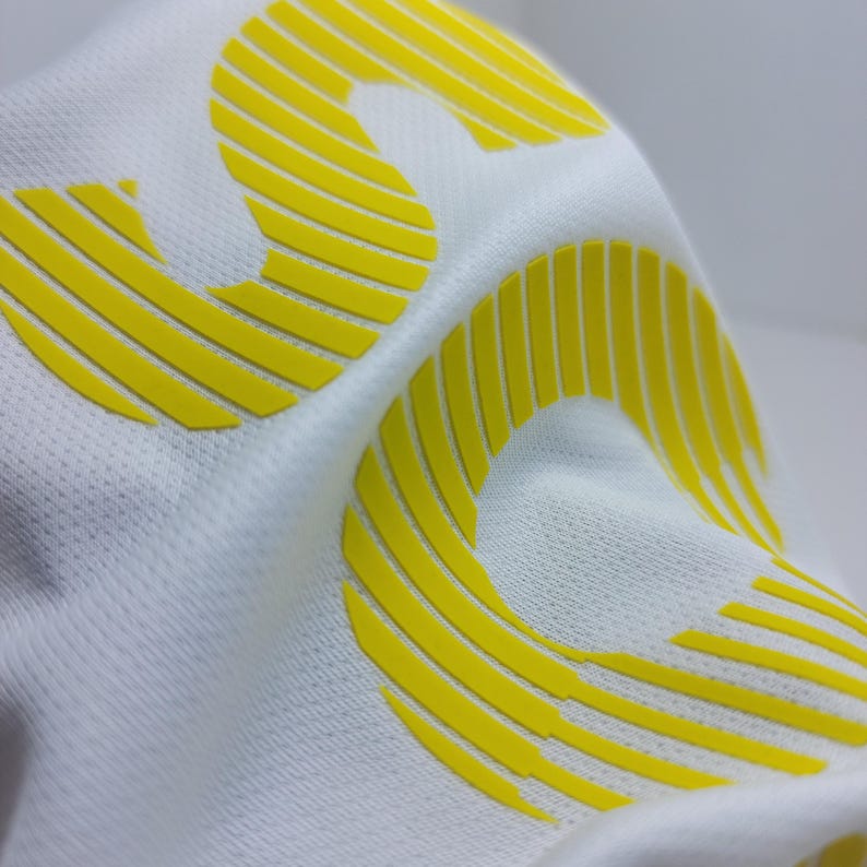 May include: White fabric with a yellow, raised, stylized number "3" printed on it.
