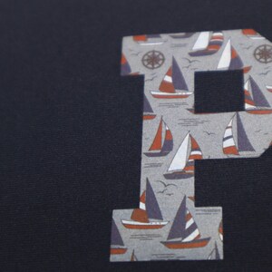 May include: A navy blue fabric with a large letter "P" cut out of the fabric. The letter "P" is printed with a pattern of sailboats and anchors.