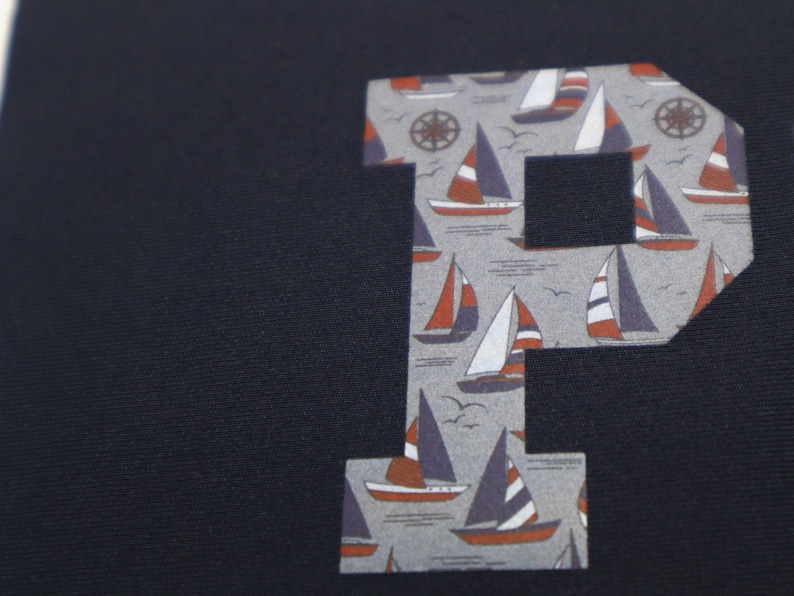 May include: A navy blue fabric with a large letter "P" cut out of the fabric. The letter "P" is printed with a pattern of sailboats and anchors.