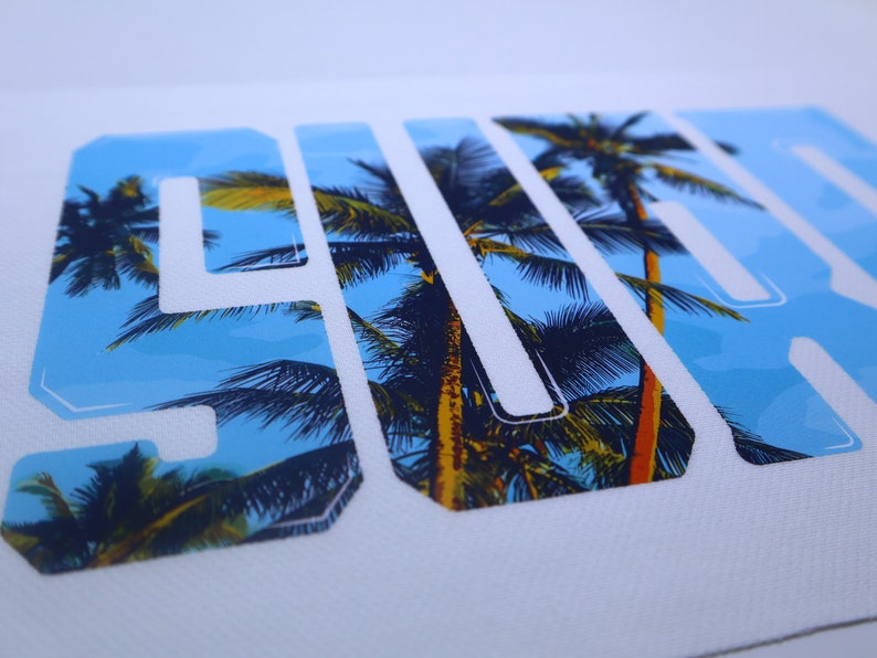 May include: White t-shirt with a graphic print of the word "SURF" in white letters with a tropical palm tree design.