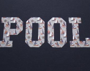 May include: The word "POOL" is spelled out in white letters with a nautical pattern of sailboats and anchors. The letters are cut out of a dark blue fabric.