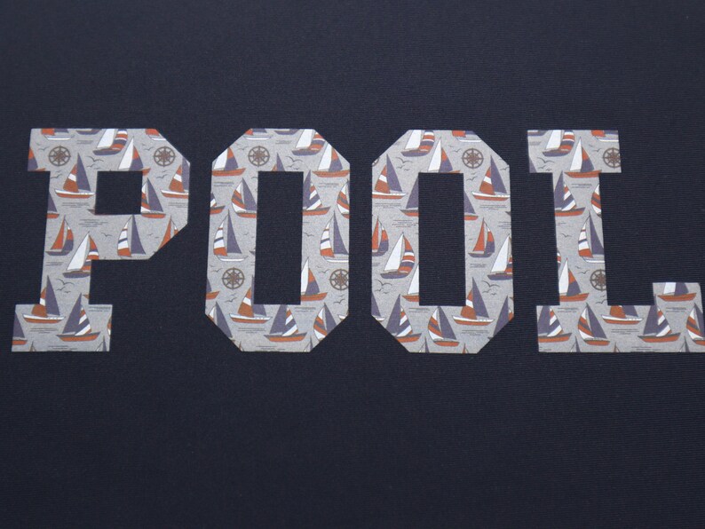May include: The word "POOL" is spelled out in white letters with a nautical pattern of sailboats and anchors. The letters are cut out of a dark blue fabric.