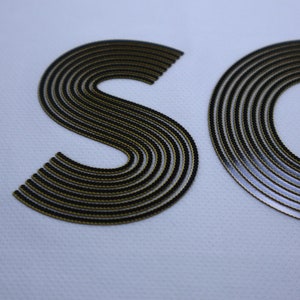 Pode incluir: Close-up de um logotipo "SO" preto e dourado com um design texturizado e em camadas.