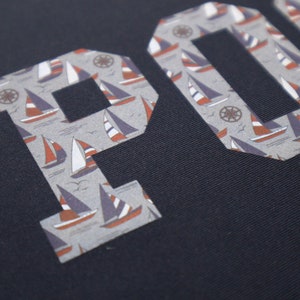 May include: A navy blue fabric with the word "POLO" in white letters. The letters are filled with a pattern of small sailboats and anchors.