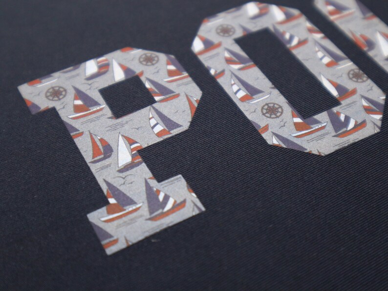 May include: A navy blue fabric with the word "POLO" in white letters. The letters are filled with a pattern of small sailboats and anchors.