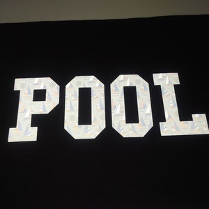May include: White reflective fabric patch with the word "POOL" in large, bold letters. The letters are filled with a pattern of small sailboats.