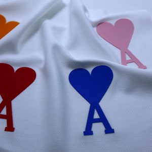 May include: Four heart-shaped patches with the letter 'A' in the center. The hearts are orange, red, blue, and pink. The patches are on a white fabric background.
