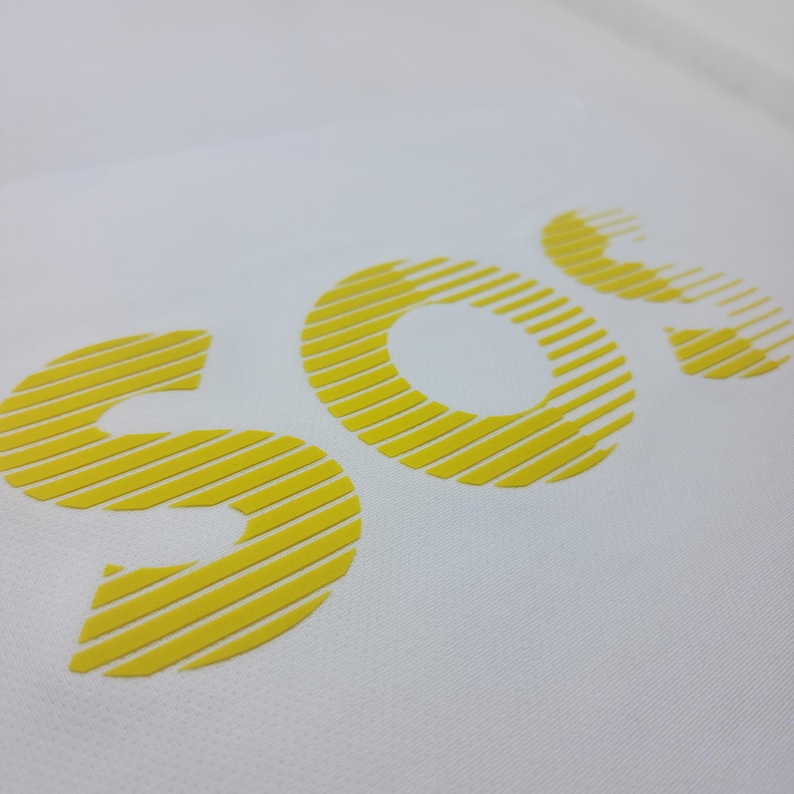 May include: White t-shirt with the word "SOC" printed in yellow with a striped pattern.