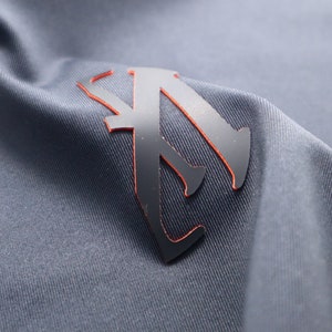 May include: A black and orange logo with a stylized letter "A" on a gray fabric background.