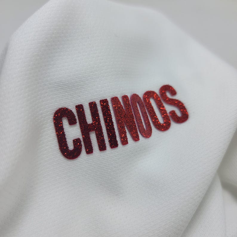 May include: White fabric with the word "CHINOOS" in red glitter lettering.