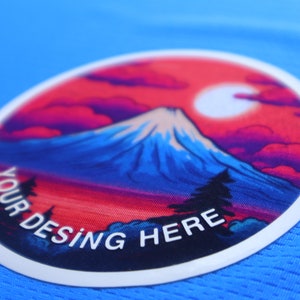 K&ouml;nnte beinhalten: Ein wei&szlig;er runder Patch mit einem bunten Bild einer Bergkette und einem roten Himmel. Der Text "YOUR DESING HERE" ist in Wei&szlig; auf dem Patch gedruckt.