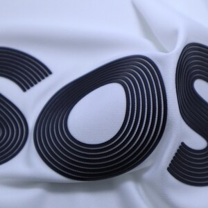 May include: White fabric with the word "SOS" printed in black, with each letter made up of multiple overlapping lines.