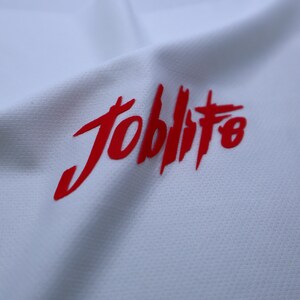 Puede incluir: Camiseta blanca con un logotipo rojo "Joblife" impreso en la parte delantera.