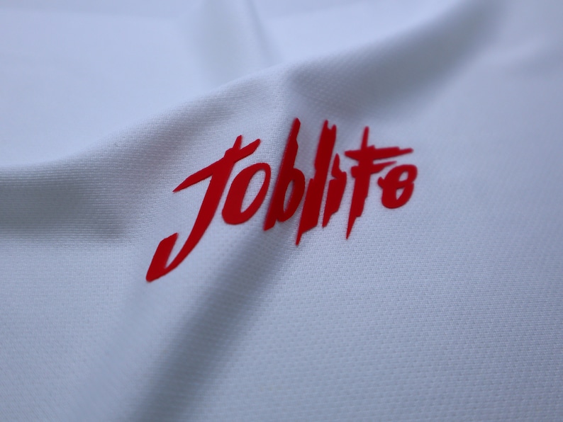 Puede incluir: Camiseta blanca con un logotipo rojo "Joblife" impreso en la parte delantera.