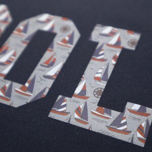 May include: A navy blue fabric with the word "COOL" printed in white letters. The letters are filled with a pattern of small sailboats.
