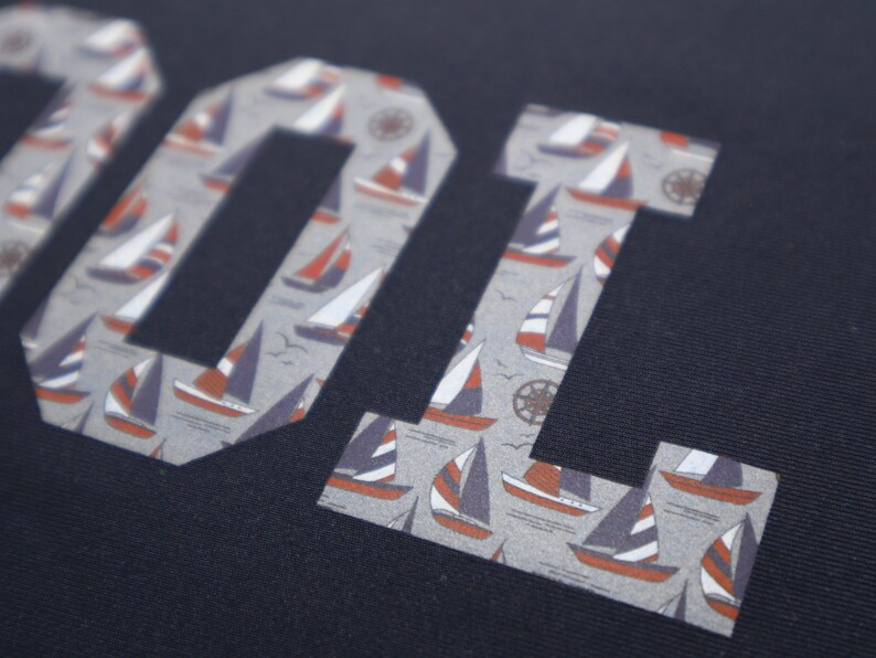 May include: A navy blue fabric with the word "COOL" printed in white letters. The letters are filled with a pattern of small sailboats.