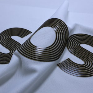 Pode incluir: Tecido branco com a palavra "SOS" impressa em preto e dourado. O tecido est&aacute; dobrado, criando um efeito tridimensional.