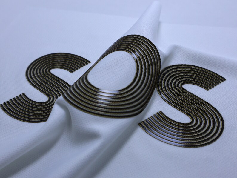 Pode incluir: Tecido branco com a palavra "SOS" impressa em preto e dourado. O tecido est&aacute; dobrado, criando um efeito tridimensional.