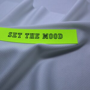 May include: A white fabric with a bright yellow label that says "SET THE MOOD" in black text.