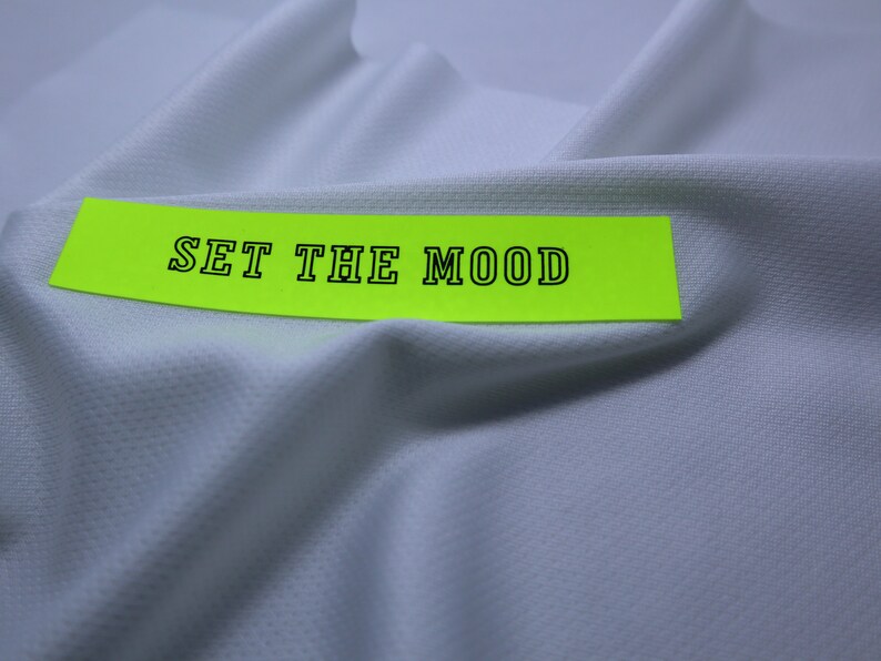 May include: A white fabric with a bright yellow label that says "SET THE MOOD" in black text.