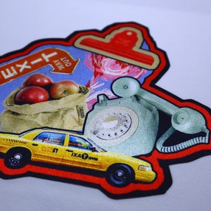 Peut inclure: Un patch color&eacute; avec une bordure rouge, repr&eacute;sentant un taxi jaune, un t&eacute;l&eacute;phone &agrave; cadran vert, un sac de pommes rouges et un panneau bleu avec le texte "Sortie" et une fl&egrave;che pointant vers la droite. Le panneau indique &eacute;galement "Out Way".