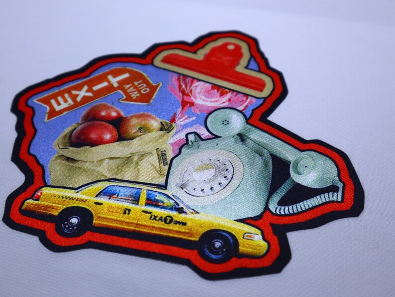 Peut inclure: Un patch color&eacute; avec une bordure rouge, repr&eacute;sentant un taxi jaune, un t&eacute;l&eacute;phone &agrave; cadran vert, un sac de pommes rouges et un panneau bleu avec le texte "Sortie" et une fl&egrave;che pointant vers la droite. Le panneau indique &eacute;galement "Out Way".