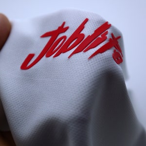 Puede incluir: Camiseta deportiva blanca con un logotipo "Joptix" rojo impreso en la parte delantera.