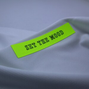 May include: A bright yellow sticker with black text that reads "SET THE MOOD" on a white fabric background.