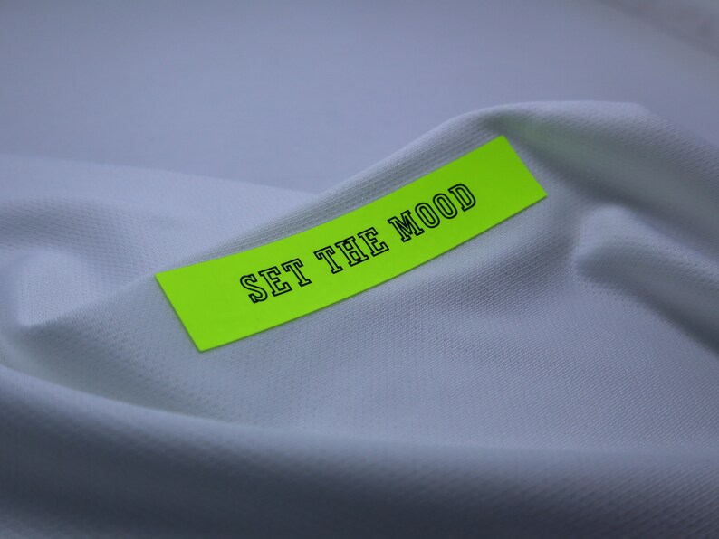 May include: A bright yellow sticker with black text that reads "SET THE MOOD" on a white fabric background.